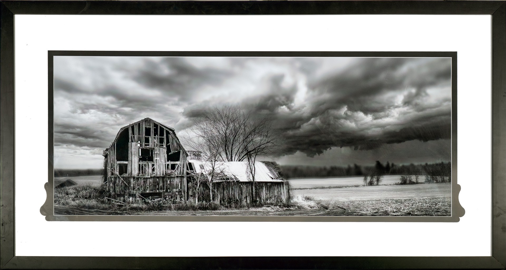 Framed monochrome photograph of weathered barns beneath storm clouds